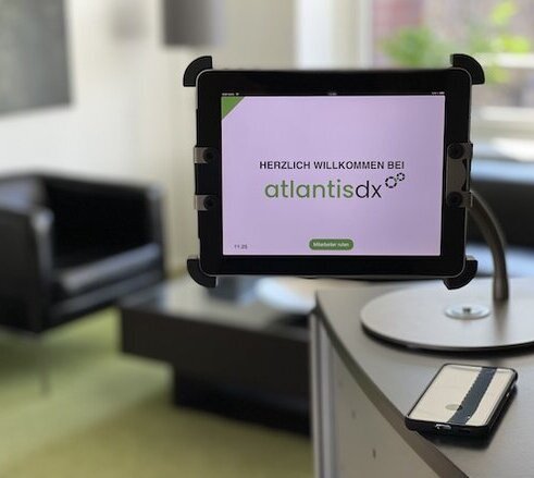 atlantis dx - Kontakt Foto: Tresen im Eingangsbereich von atlantis dx mit Tablet, Nahaufnahme vom Tablet mit Begrüßungstext Herzlich willkommen bei atlantis dx