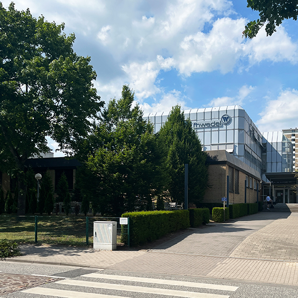 Foto: Gebäude der FH Wedel von schräg vorne, Bäume und blauer Himmel