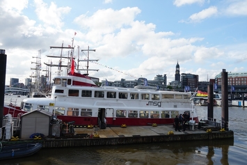 atlantis dx - 25 Jahre Firmenjubiläum Foto: Ein Schiff an den Hamburger Landungsbrücken mit Blick auf die Stadt und Himmel