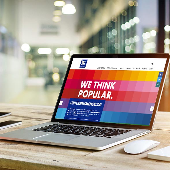 atlantis dx - Bauer Media Group: Abonnement-Shop mit Magento 2 Foto: seitliche Ansicht auf Laptop mit geöffneter Website der Bauer Media Group, Holztisch, weiße Mouse neben dem Laptop